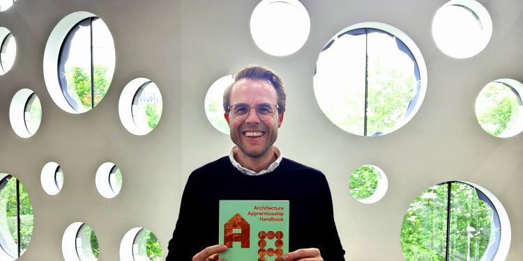 Luke Murray smiles holding a copy of the Architecture Apprenticeship Handbook